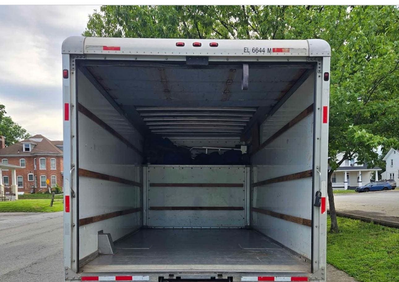 Open rear of a box truck with a few bags inside, parked on a residential street.