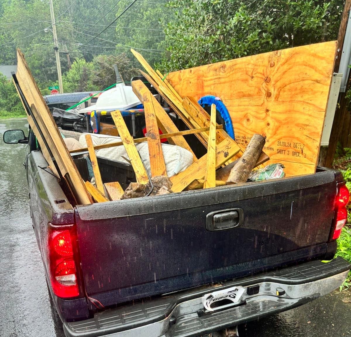 Pickup bed in the rain, loaded with plywood, framing lumber, and a log.